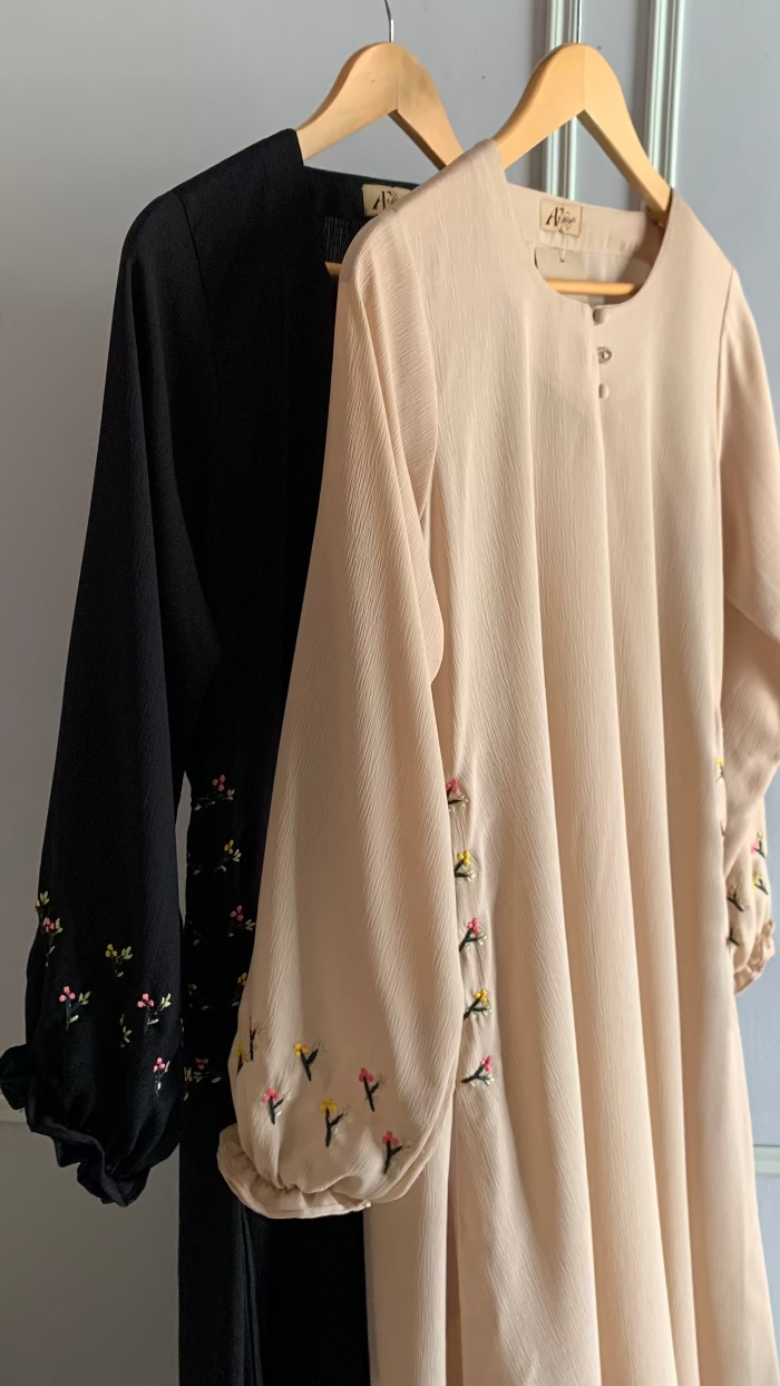 Black and beige long-sleeve shirts with floral embroidery on hangers against a light gray wall.