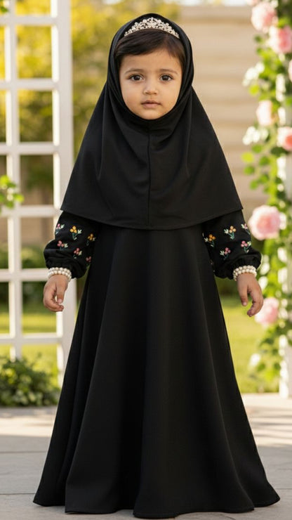 Young girl in a black dress with floral embellishments standing in front of a decorative floral arch.