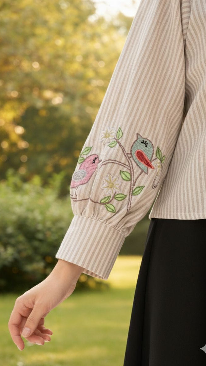 Beige ribbed sweater with embroidered birds on a blurred green outdoor background