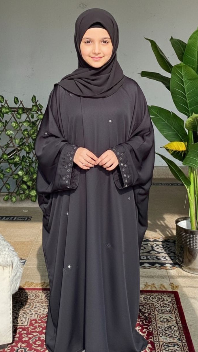 Woman wearing a dark gray abaya with a hijab in a home setting.
