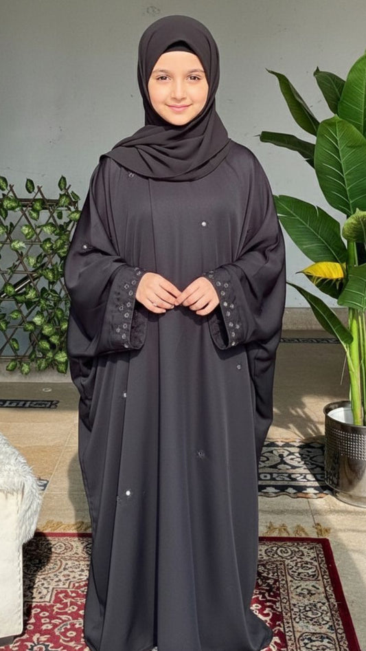 Woman wearing a dark gray abaya with a hijab in a home setting.