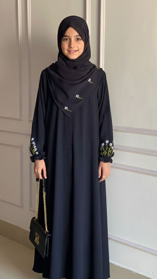 Woman wearing a dark blue dress with floral patterns against a neutral wall.