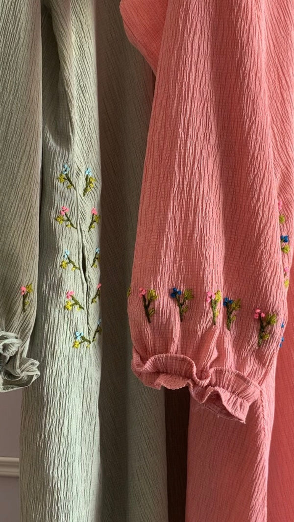 Two pairs of pants, one green and one pink, with floral embroidery on cuffs against a neutral background.