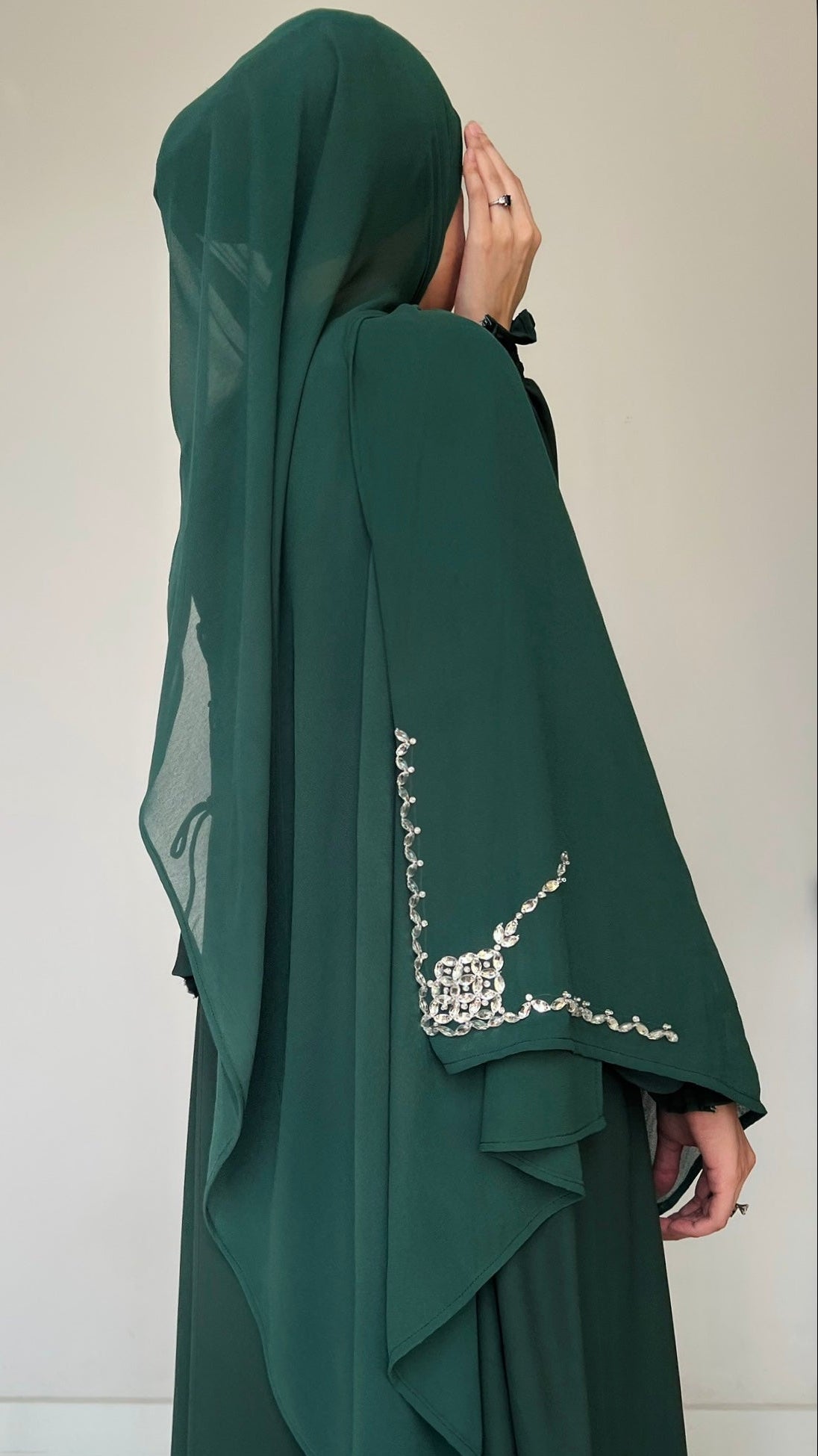 Person wearing a green abaya with intricate detailing on a white background