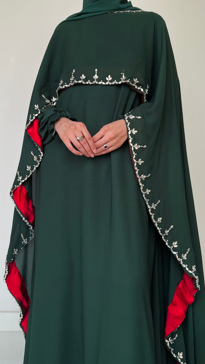 Green abaya with red accents and intricate white embroidery on a plain background