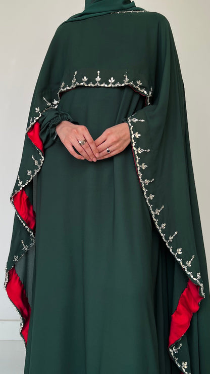 Green abaya with red accents and intricate white embroidery on a plain background