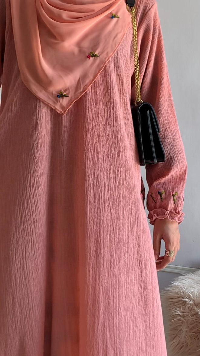 Person wearing a pink dress with a matching hijab against a neutral background