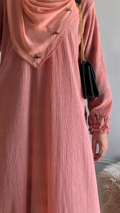 Person wearing a pink dress with a matching hijab against a neutral background