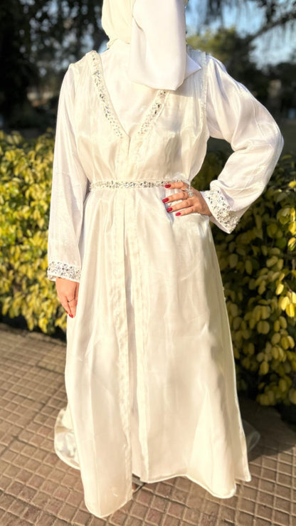 Person wearing a white dress with lace details standing outdoors near yellow bushes.